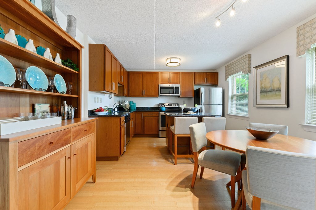 A kitchen and dining area with hardwood-style flooring, stainless steel appliances, and two windows in the Deluxe Tahoe floor plan at New Kent Apartments in West Chester, PA