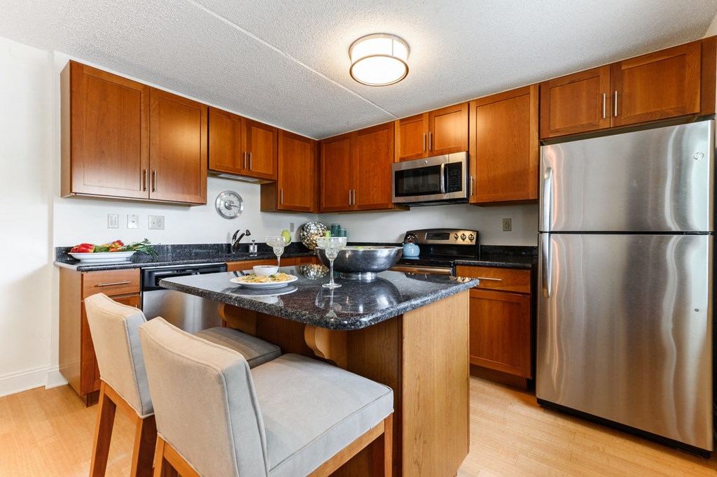 A modern L-shaped kitchen with stainless steel appliances, a kitchen island, and elegant hardwood-style flooring in the Tahoe floor plan at New Kent Apartments, West Chester, PA