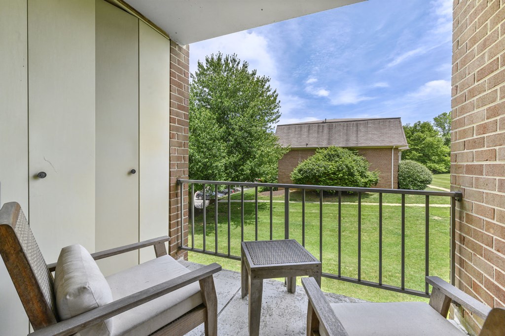 A covered balcony with two chairs, a small table, and two doors leading to a storage closet in an Aspen floor plan at New Kent Apartments, West Chester, PA