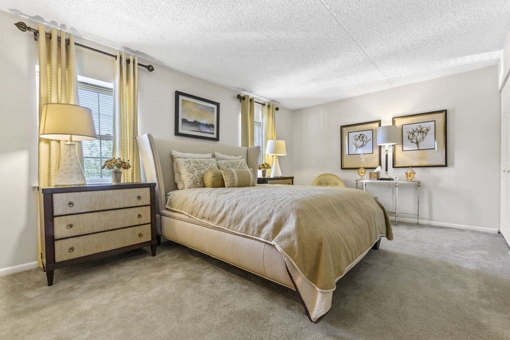 A spacious bedroom at New Kent Apartments in West Chester, PA, featuring two windows, plush carpet flooring, and soaring high ceilings