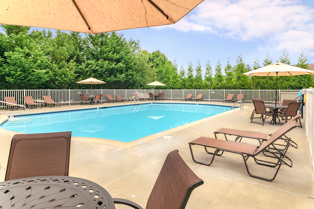 A gated resort-style pool at our Severgn Apartments in Exton, PA with lounge chairs, tables, and umbrellas surrounded by trees.