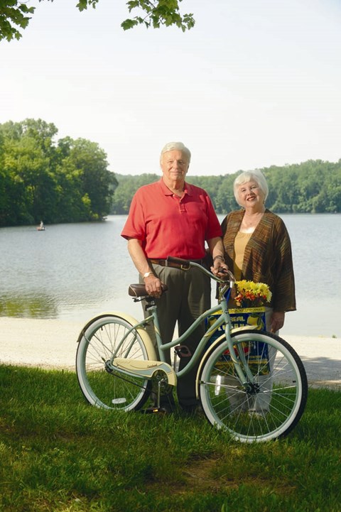 An elderly couple standing next to a green bicycle.