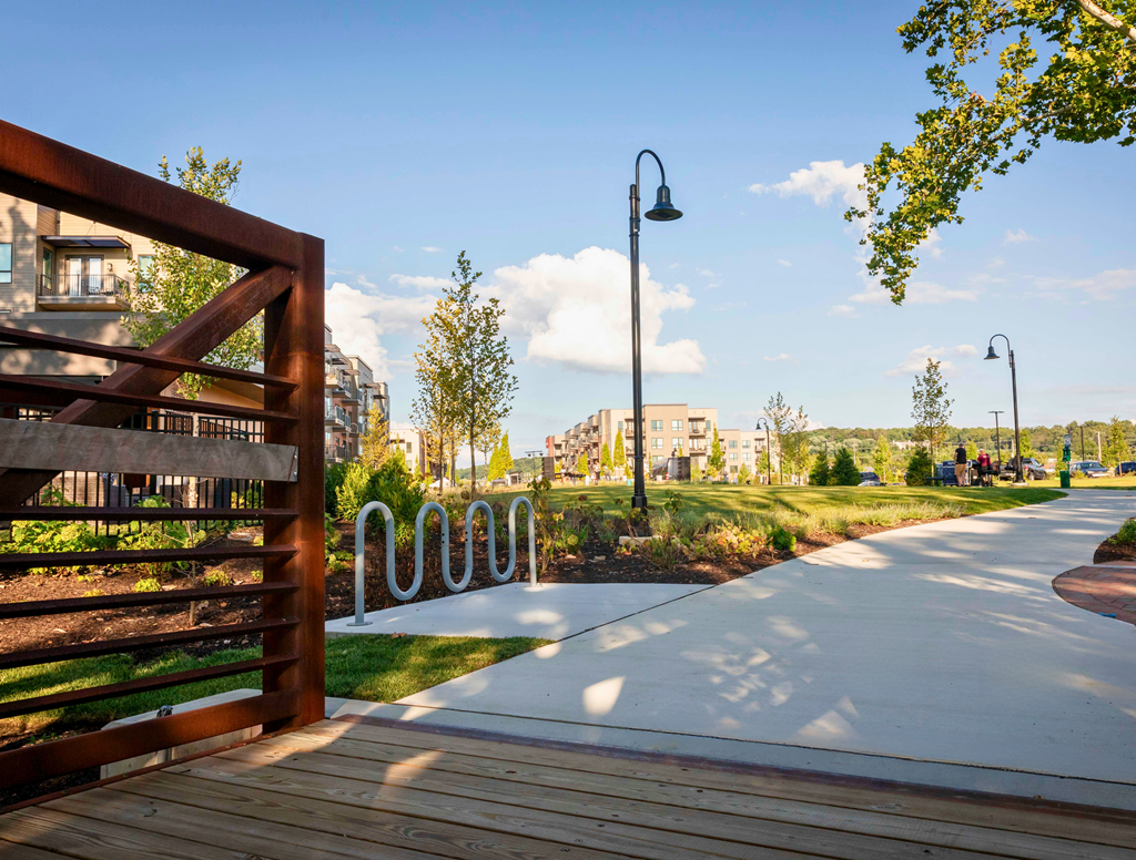 A large green space with a walking trail, path lights, trees, bike station, and bridge near River Station apartment buildings.