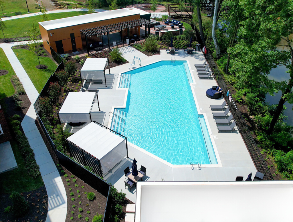 A sparkling resort-style pool near trees with lounge chairs, tables, chairs, and 3 shaded lounge areas.