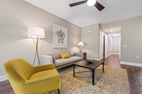 A yellow chair sits in a living room with a couch and a lamp.