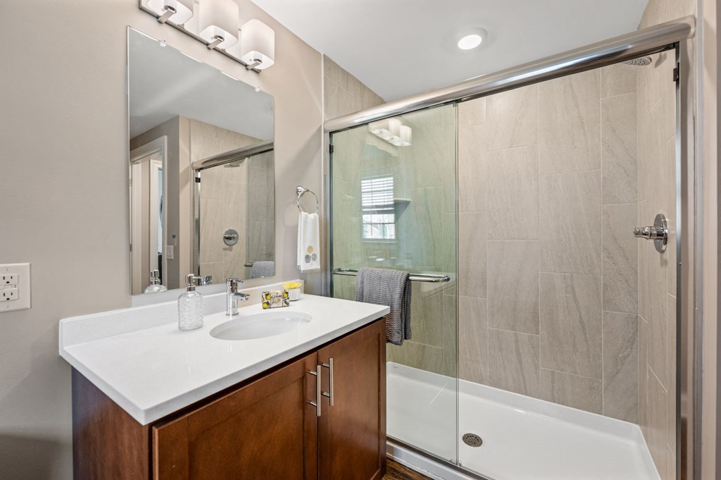 A bathroom inside an Exton apartment with vanity, large mirror, and sliding glass doors leading to a stand-up shower with tile walls.
