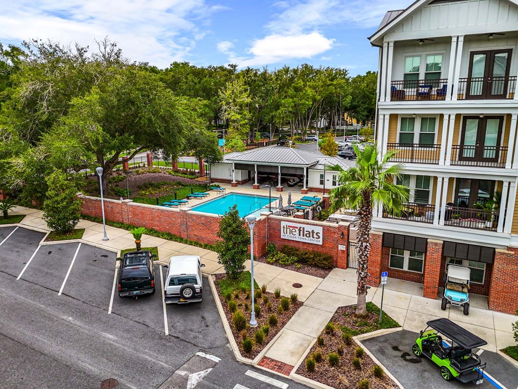 A view of a parking lot with cars and a building with a pool in the background.