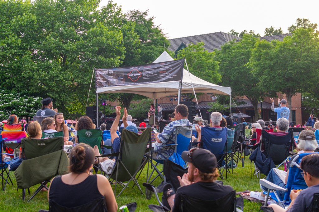 A group of people are sitting in lawn chairs under a tent, watching a speaker.