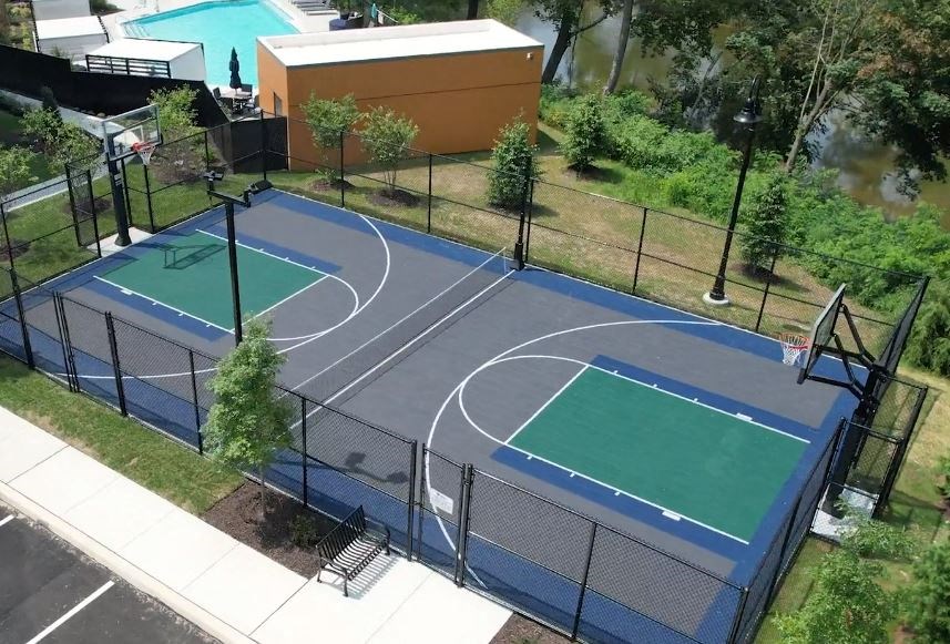 An outdoor basketball court near a gated pool and a river with trees.