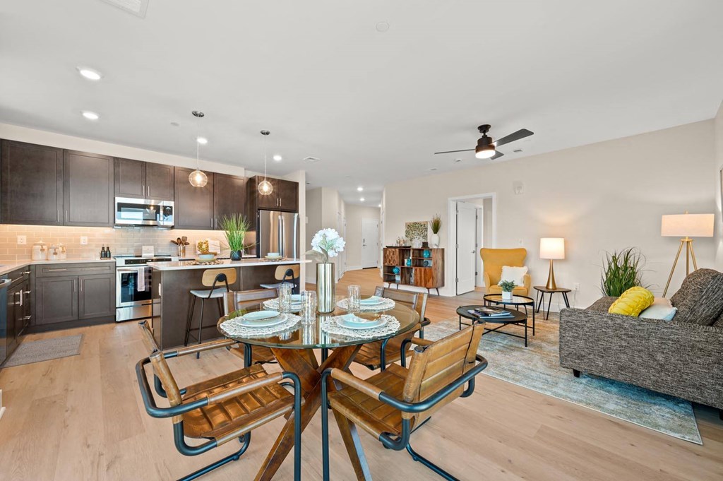 Open-concept living room and kitchen with a stylish dining table, wood-inspired flooring, and stainless steel appliances at Hamilton at Eagleview in Exton, PA