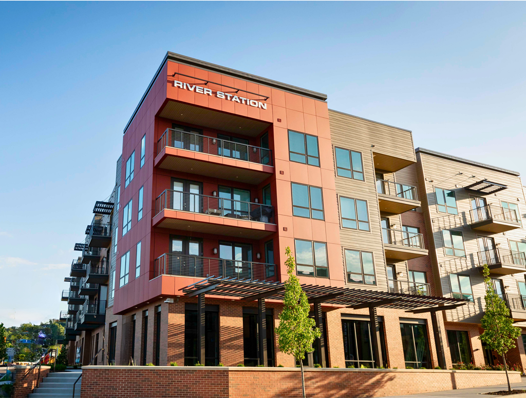 River Station's four-story apartment building with balconies and a pergola with trees on the main level.