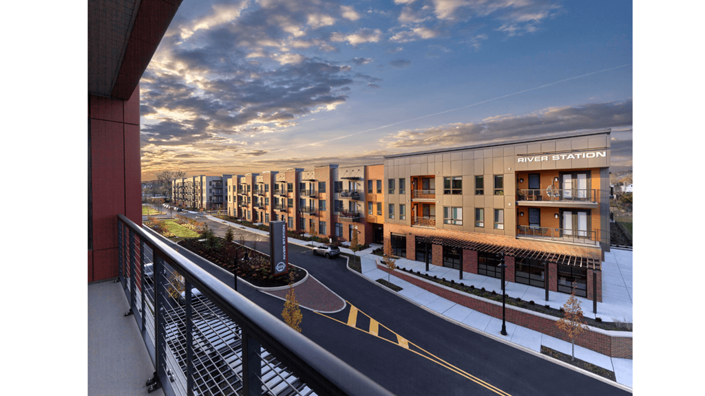 A balcony view of River Station's modern apartment building lining a street with the sun setting in the background.