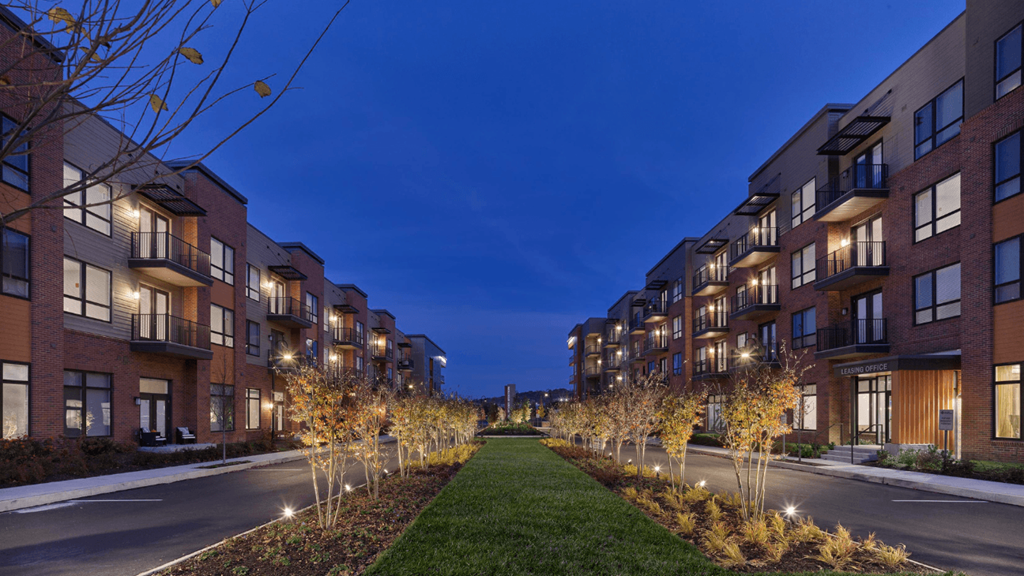 A row of River Station's apartment buildings lining each side of a street with trees and grass growing in the middle.