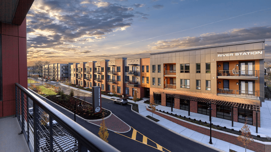 A balcony view of River Station's modern apartment building lining a street with the sun setting in the background.