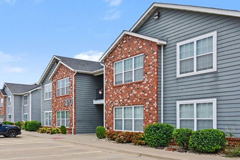 A black car is parked in front of a grey building with a brick wall.