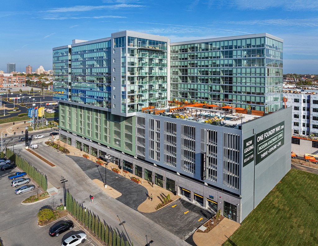 A modern glass building with a parking lot in front. at One Foundry Way Apartments, Missouri