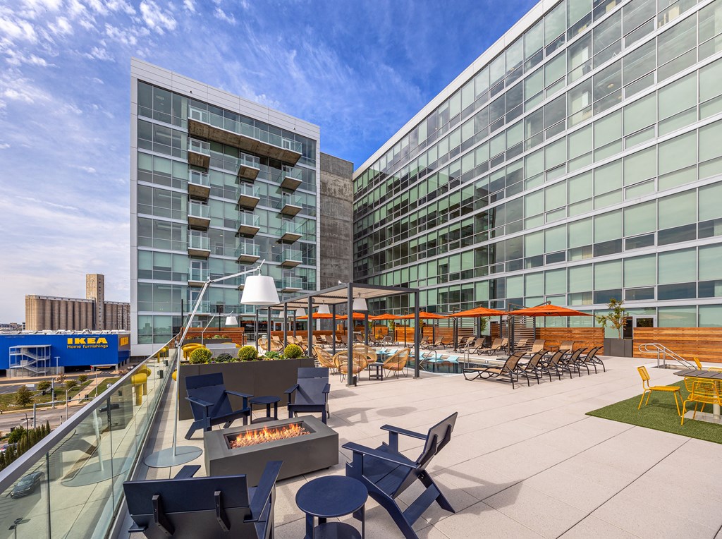 A modern building with a glass facade and a patio with chairs and tables. at One Foundry Way Apartments, St Louis, MO