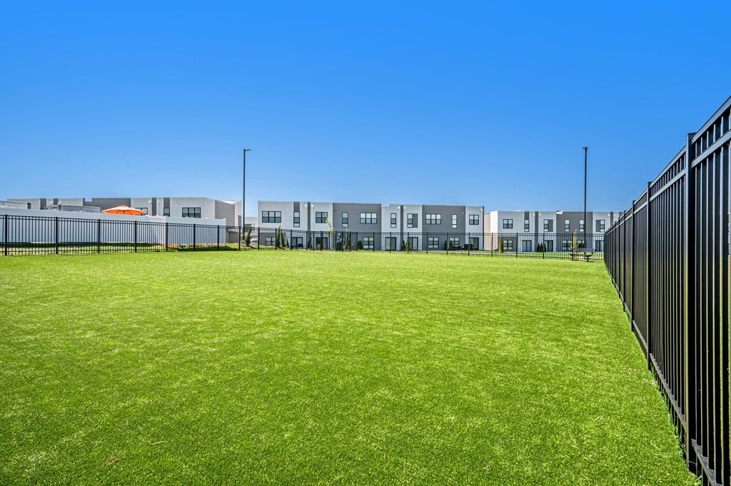 a grassy field with a fence in front of an apartment building at Signature at West Pryor, Lee's Summit, Missouri