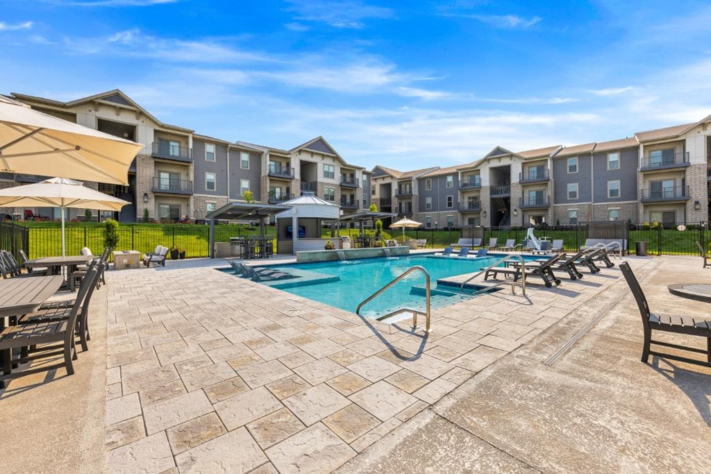 a swimming pool with chairs and umbrellas in front of an apartment building at The Prairie Luxury Apartments, Dardenne Prairie