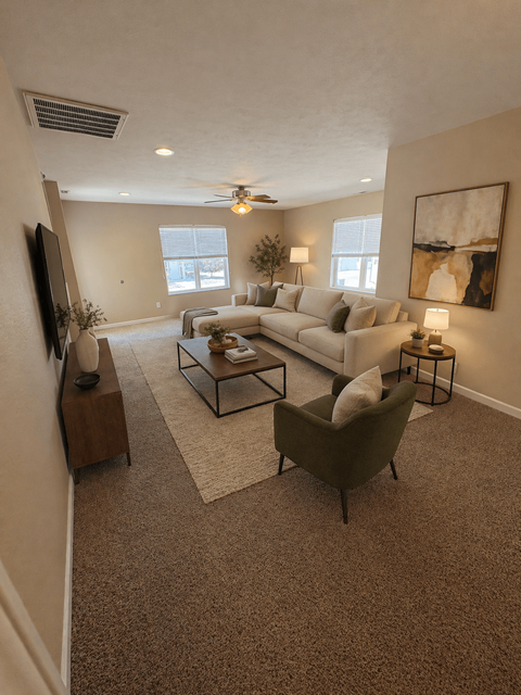 A living room with a white couch, a green armchair, and a television on the wall.