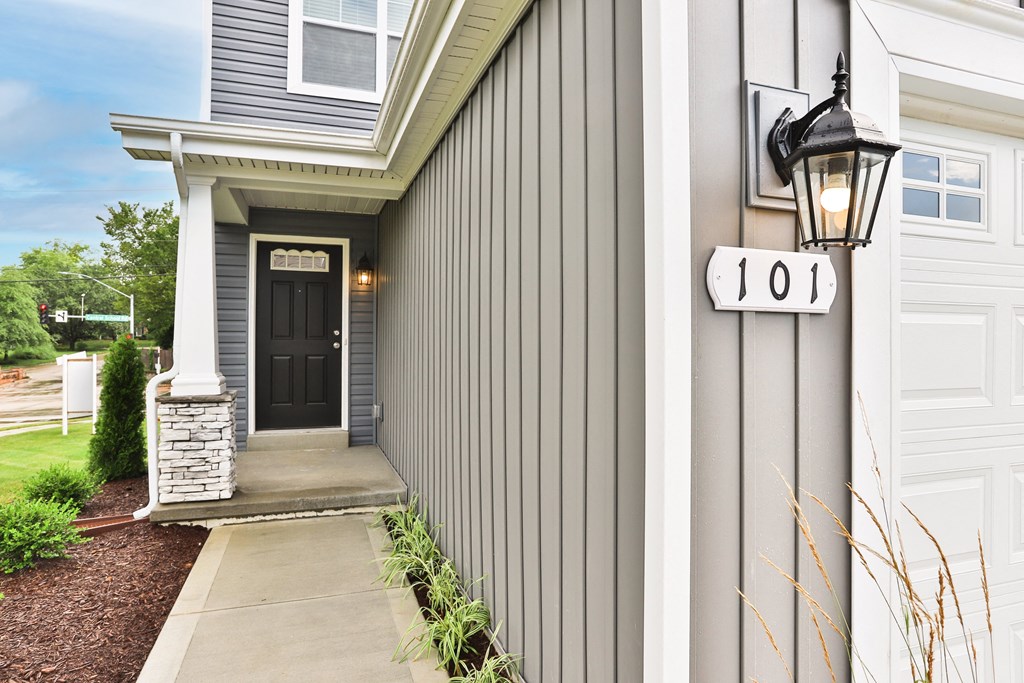 the front porch of a gray house with a black door and a street light