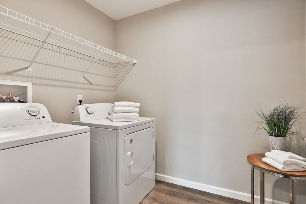 an empty laundry room with washer and dryer and a shelf with folded towels