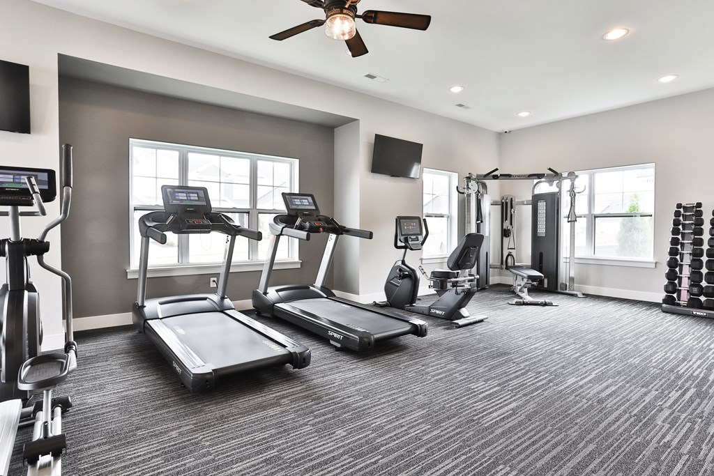 a gym with treadmills and other exercise equipment and a ceiling fan