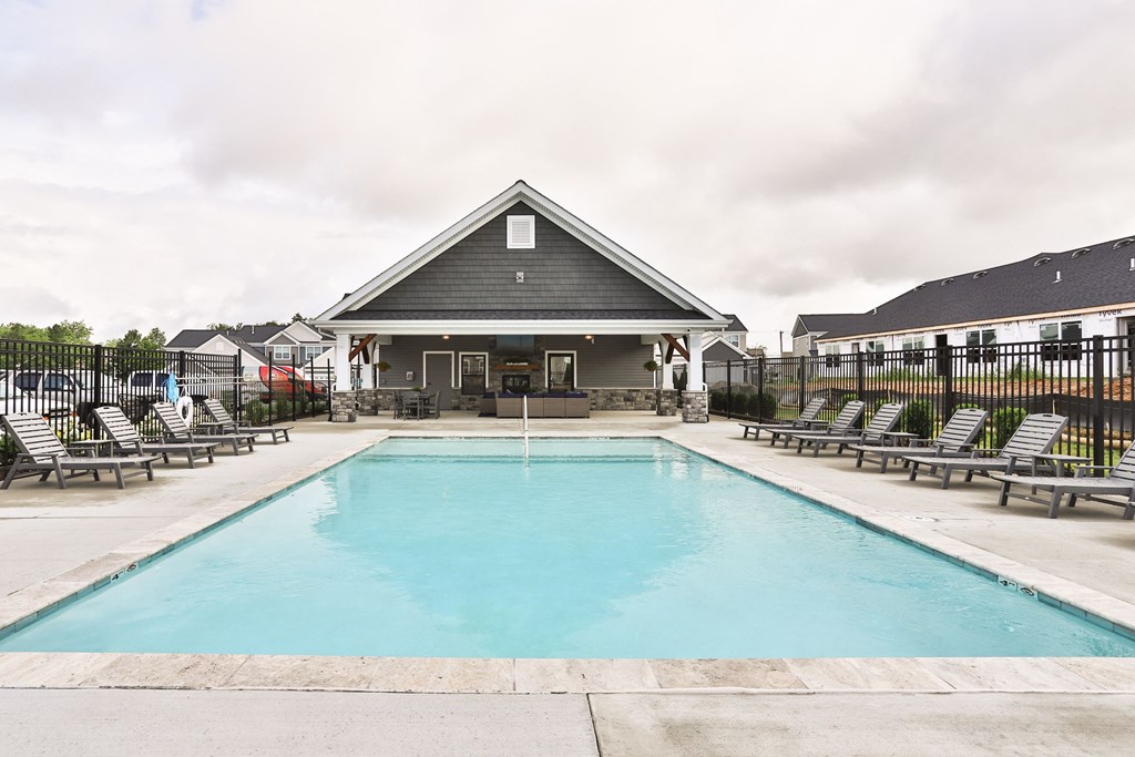 a swimming pool with chairs and a house in the background