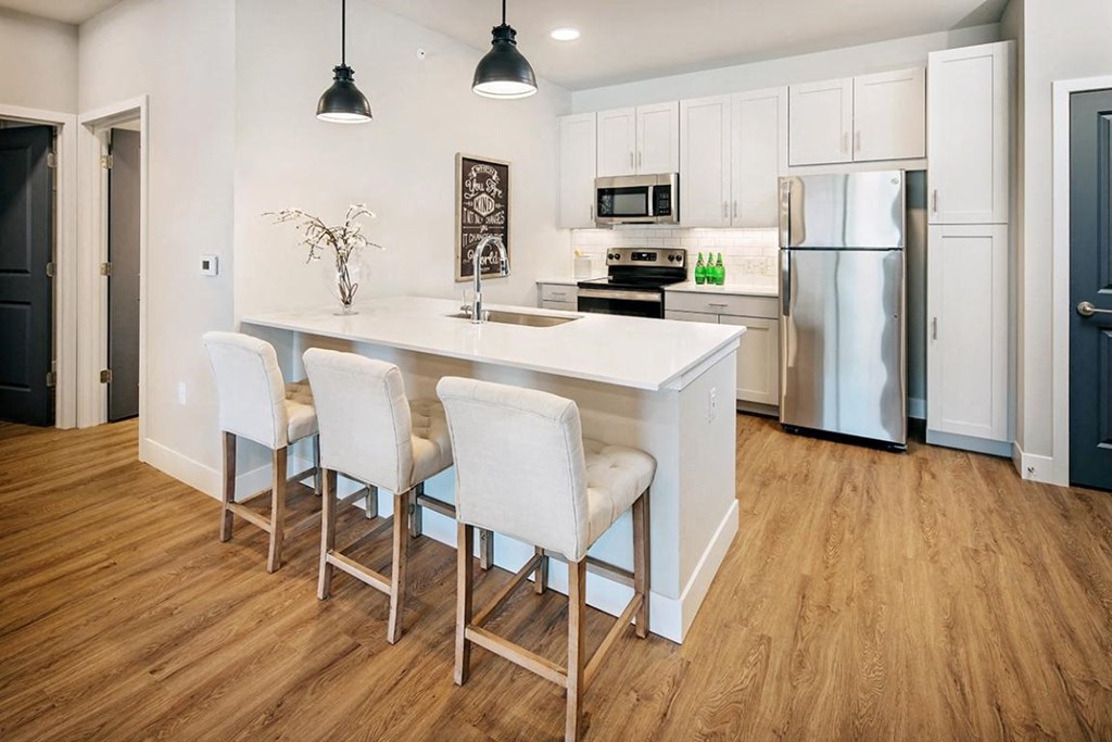 a kitchen with a large island with three white chairs at The Prairie Luxury Apartments, Missouri, 63368