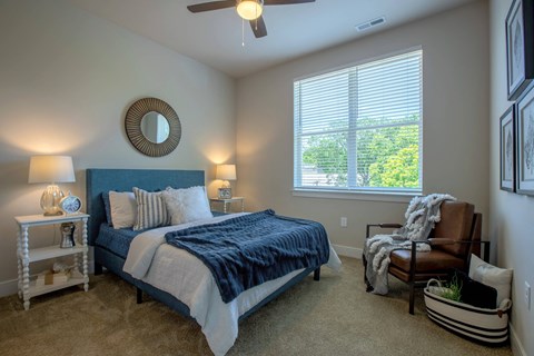 A bedroom with a bed, chair, and ceiling fan at The Elle on Lockwood Apartments, Webster Groves, Missouri