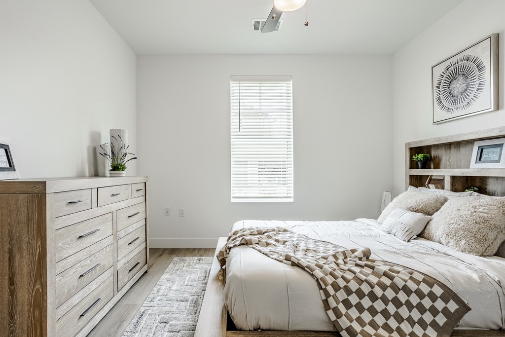 A bedroom with a bed, dresser, and window with blinds.