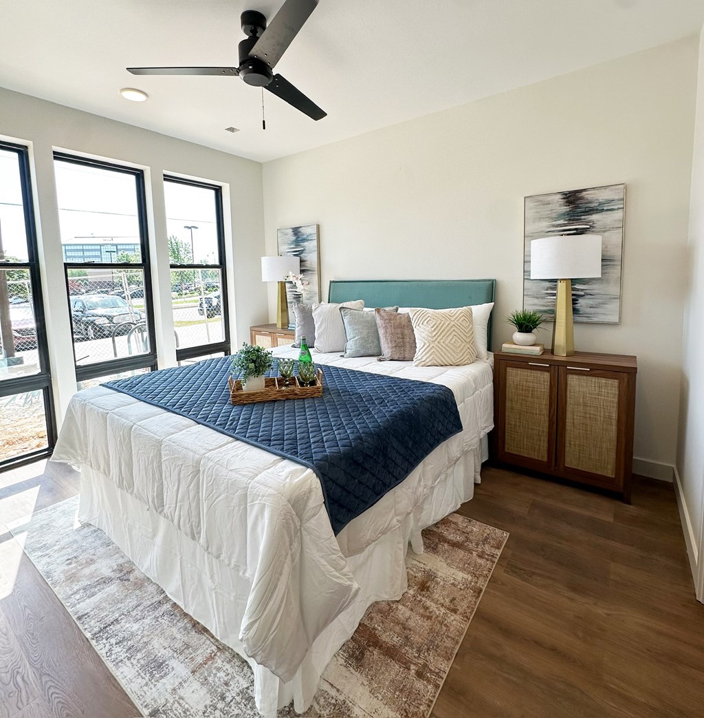 A bedroom with a bed, a ceiling fan, and a window overlooking a parking lot.