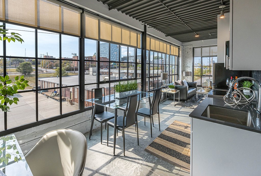 a living room with a table and chairs and a kitchen with windows