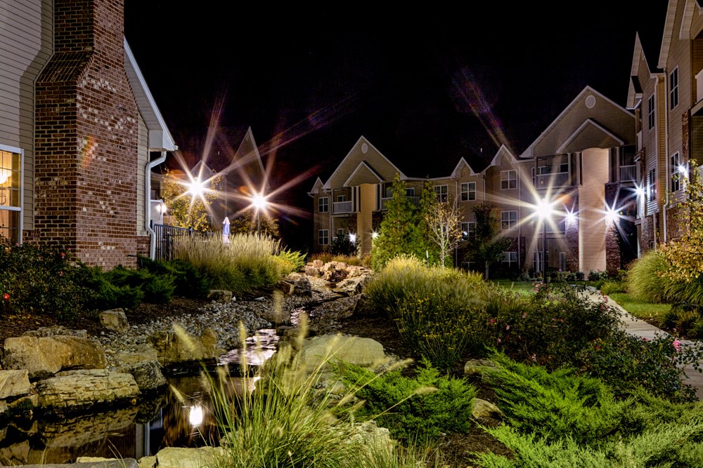 exterior photo of trees surrounded by buildings with the lights on at Villas At Crystal Lake, Illinois, 62226