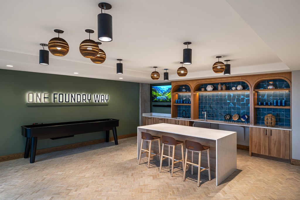 A bar area with a green wall and a neon sign that says "One Foundry Way".