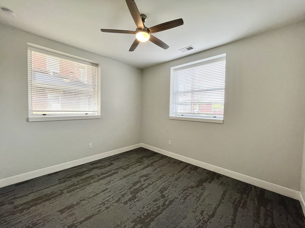 A room with a ceiling fan and two windows.