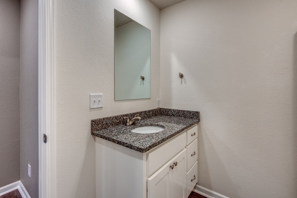 A bathroom with a granite countertop and white cabinets.