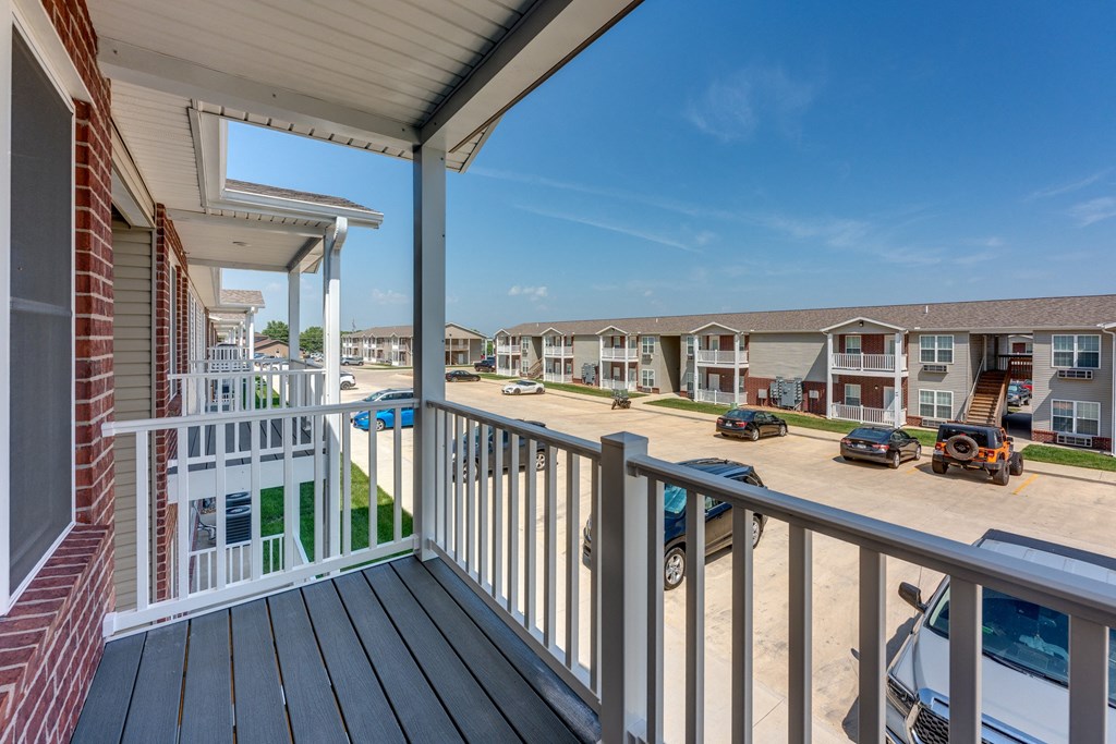 A balcony overlooks a parking lot and apartment buildings.