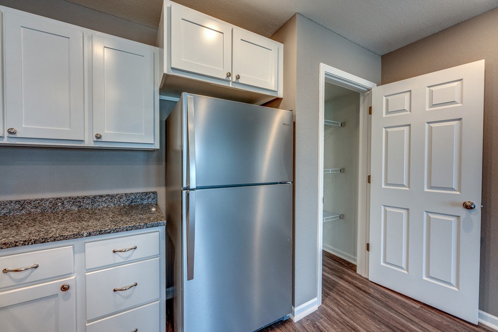 A kitchen with a refrigerator, cabinets, and a doorway leading to another room.