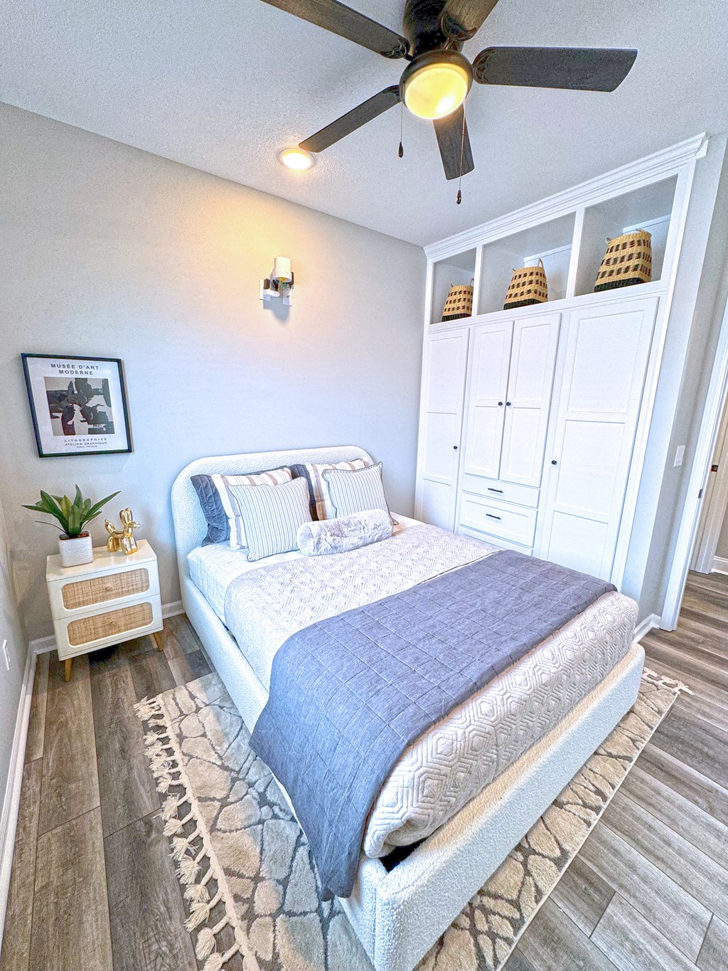 A bedroom with a bed, a ceiling fan, and a cabinet with baskets on top.