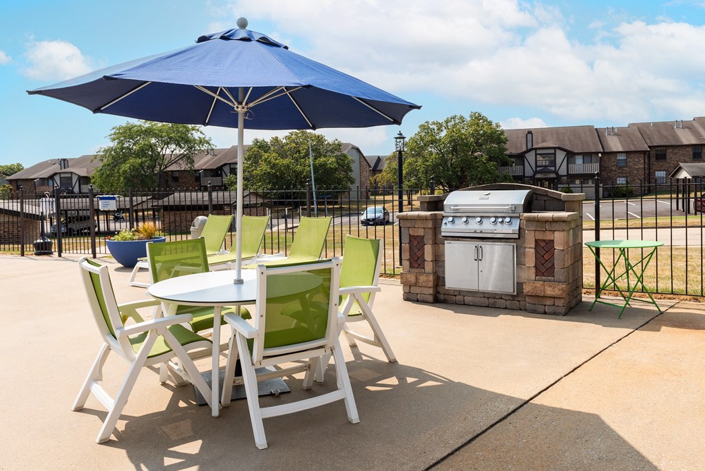 a patio with a table and chairs with an umbrella and a grill