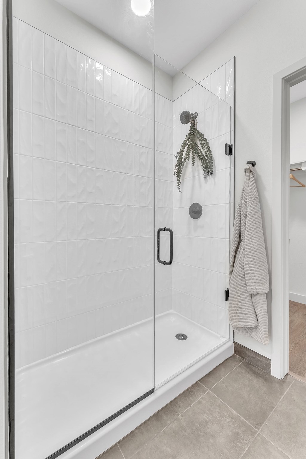 A white tiled shower with a glass door and a grey towel hanging on the door.