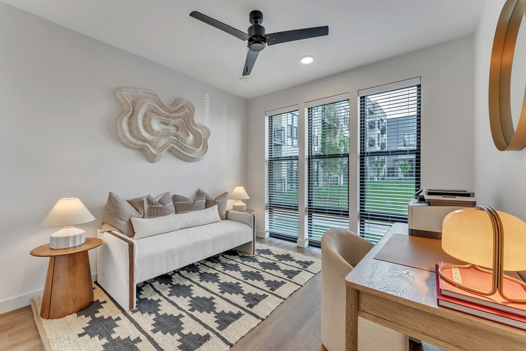 A living room with a white couch, a ceiling fan, and a table with a lamp and books.