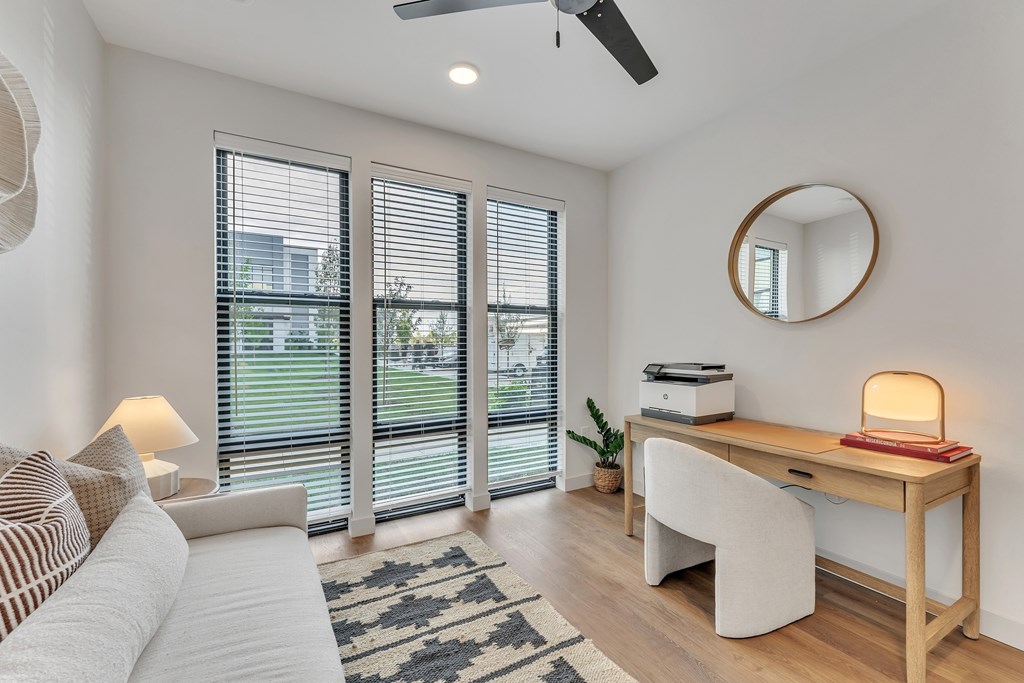 A room with a white couch, a desk with a lamp, and a round mirror on the wall.
