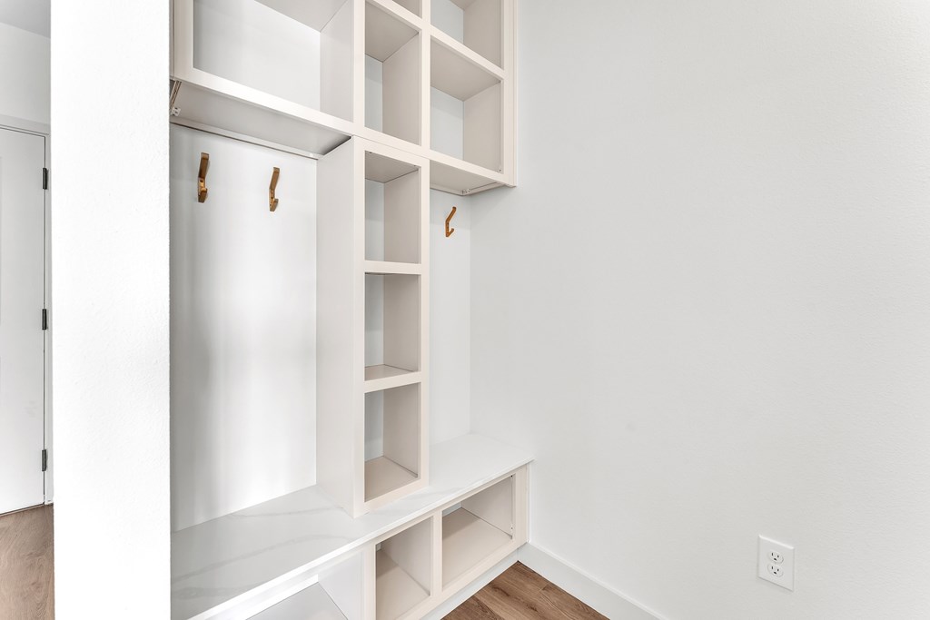 A white shelving unit with three shelves and three hooks on the door.