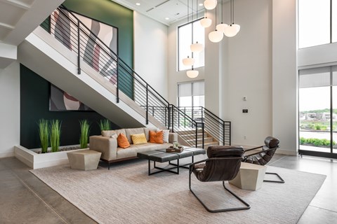 a living room with a couch and a chair in front of a staircase at The Flats & Terraces at Wildhorse Village, Chesterfield, MO