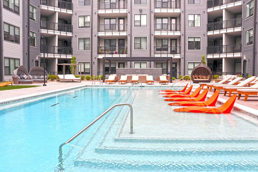 a swimming pool with orange chairs in front of an apartment building