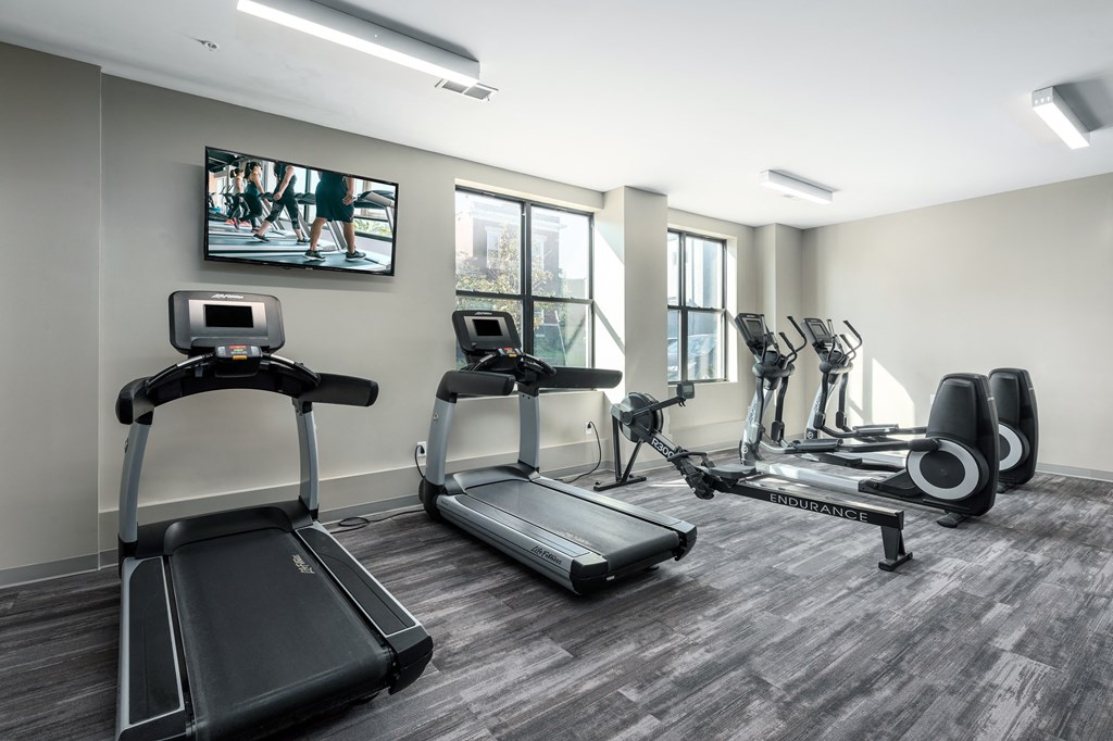 a gym with various cardio machines and a tv on the wall at Hibernia Apartments, St Louis, MO, 63139