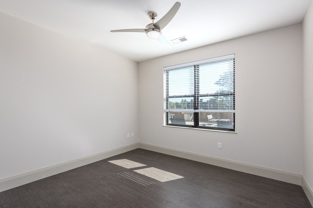 Hibernia bedroom with rich vinyl plank flooring, oversized windows with white blinds and ceiling fan at Hibernia Apartments, St Louis, Missouri