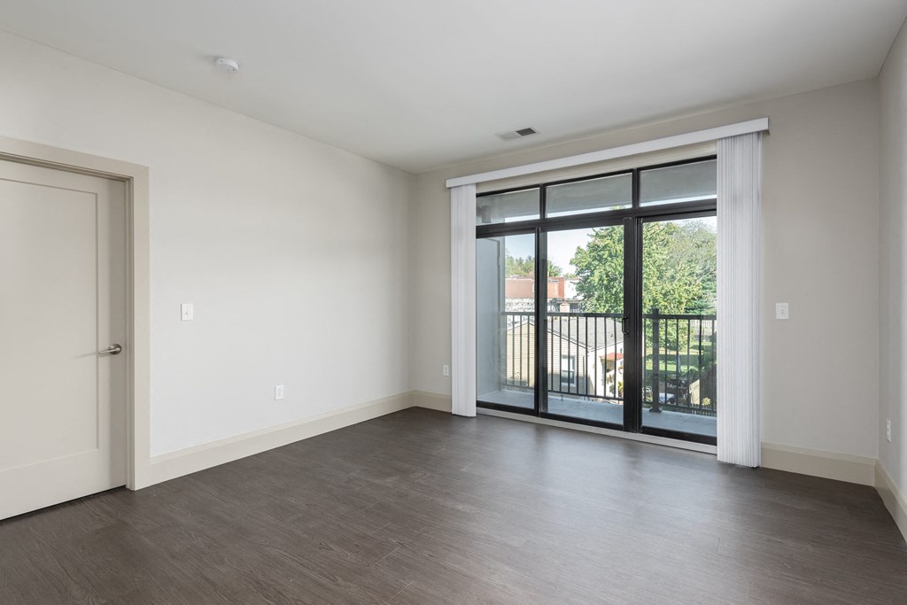 Hibernia living room with rich vinyl plank flooring and large sliding glass doors with custom window coverings leading out to a private balcony at Hibernia Apartments, St Louis, MO, 63139